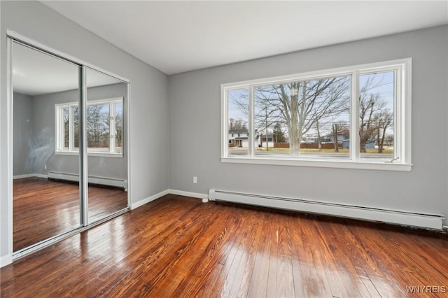 unfurnished bedroom featuring a closet, wood-type flooring, baseboards, and baseboard heating