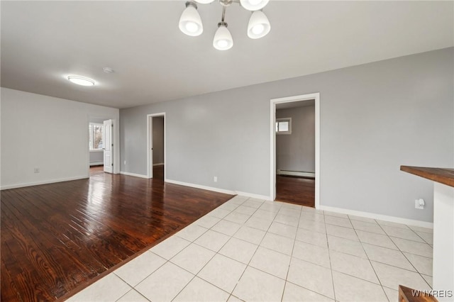 unfurnished room with light tile patterned floors, a baseboard radiator, an inviting chandelier, and baseboards