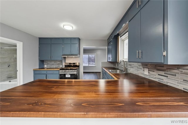 kitchen featuring blue cabinets, under cabinet range hood, a sink, wooden counters, and stainless steel range with gas cooktop