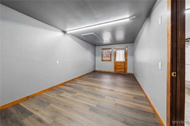 empty room with wood finished floors, attic access, and baseboards