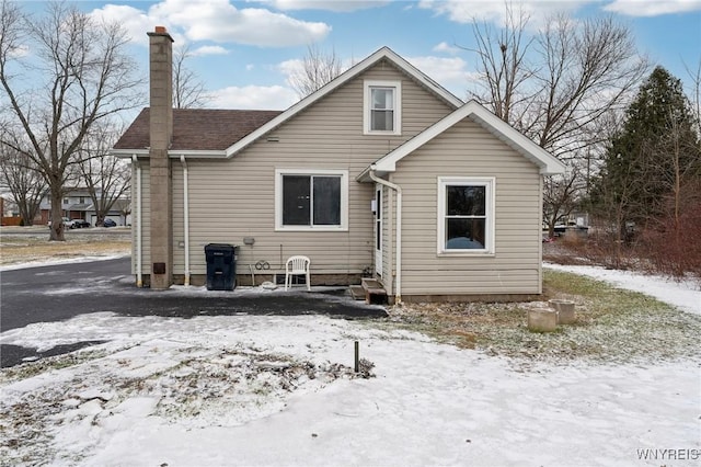 snow covered rear of property featuring a shingled roof and a chimney