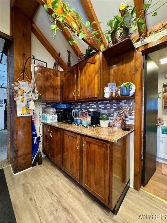 kitchen featuring lofted ceiling with beams, brown cabinets, light countertops, light wood-style floors, and backsplash