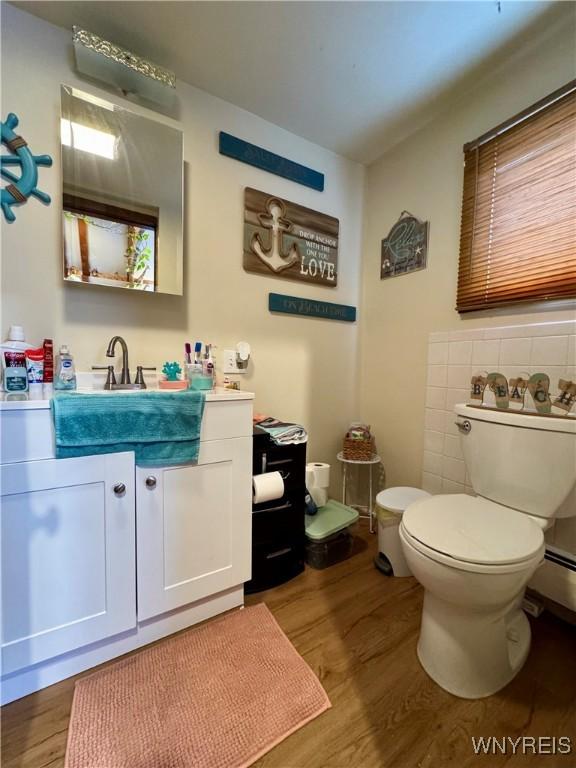 half bathroom with toilet, tile walls, wood finished floors, and vanity