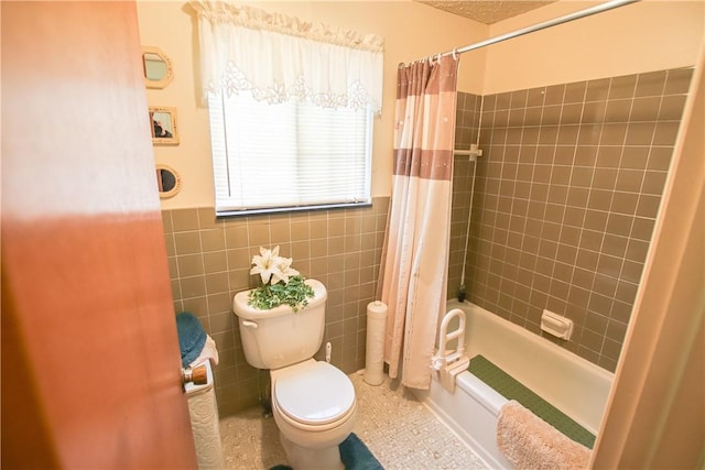 bathroom with toilet, shower / bath combo with shower curtain, tile walls, and wainscoting