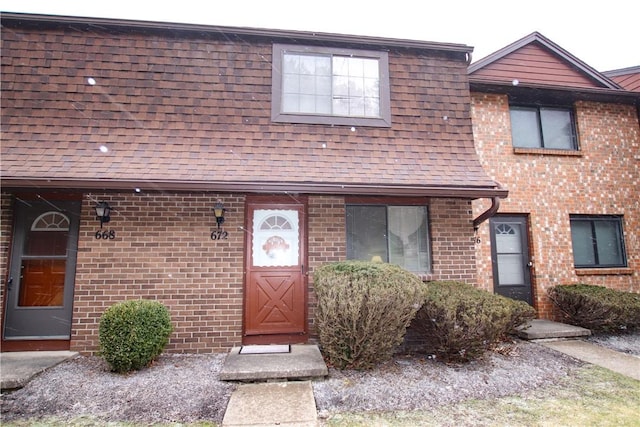 townhome / multi-family property with roof with shingles and brick siding