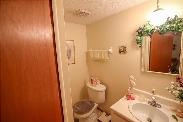 half bath featuring toilet, visible vents, a textured ceiling, and vanity