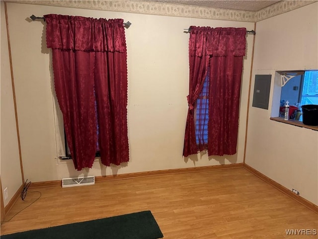 empty room featuring electric panel, visible vents, baseboards, and wood finished floors