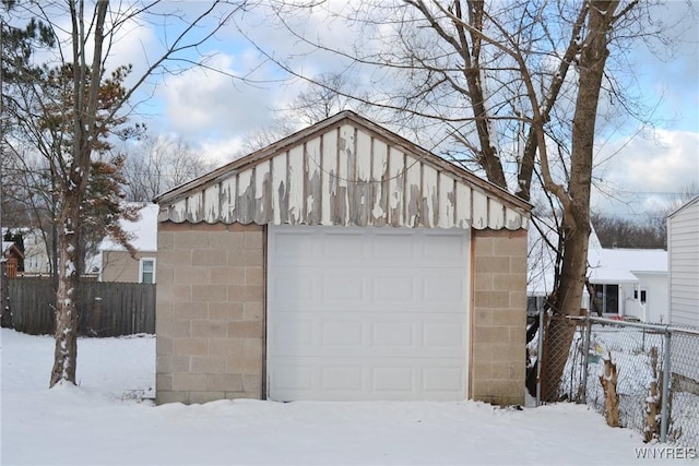 snow covered garage featuring a garage and fence