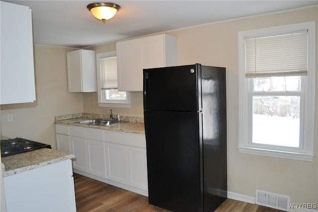 kitchen featuring visible vents, wood finished floors, freestanding refrigerator, white cabinetry, and a sink