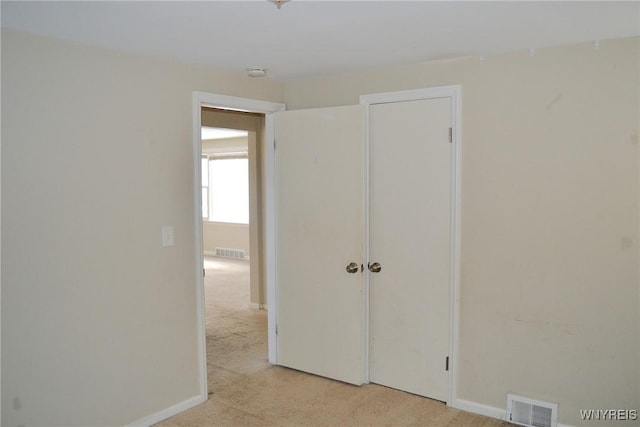 unfurnished bedroom with baseboards, visible vents, a closet, and light colored carpet