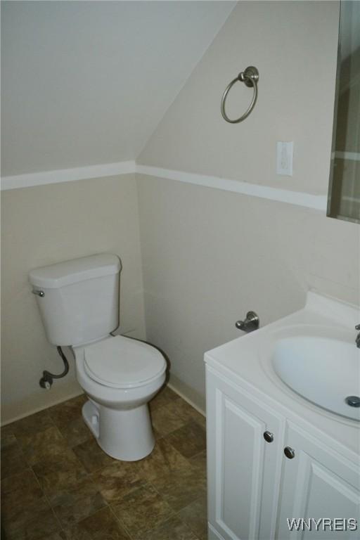 half bath featuring lofted ceiling, toilet, and vanity