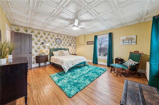 bedroom with wallpapered walls, baseboards, an ornate ceiling, ceiling fan, and light wood-style floors