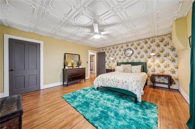 bedroom with a ceiling fan, baseboards, light wood finished floors, an ornate ceiling, and wallpapered walls