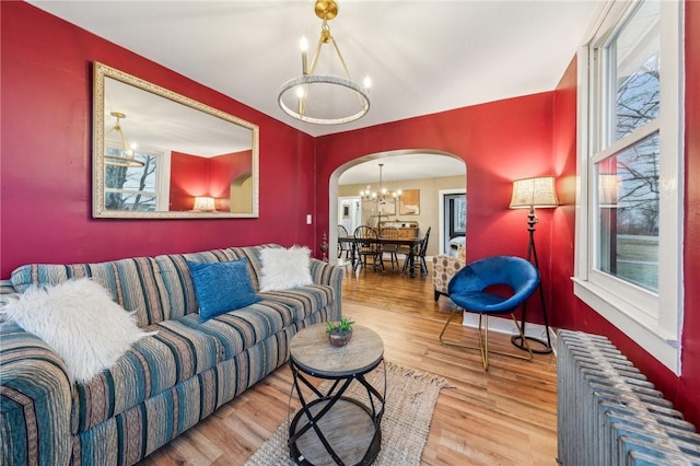 living area with an inviting chandelier, radiator heating unit, arched walkways, and wood finished floors