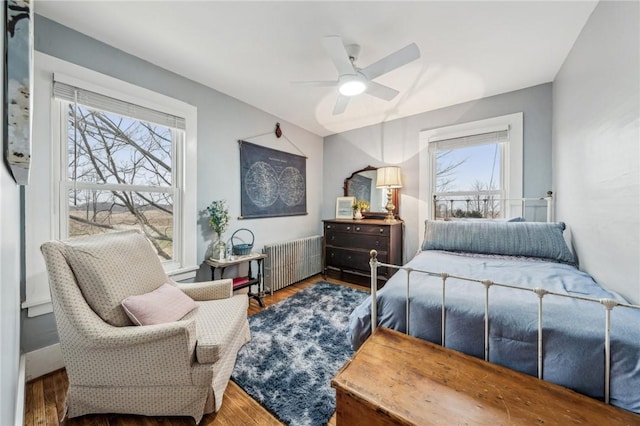 bedroom with ceiling fan, radiator heating unit, and wood finished floors