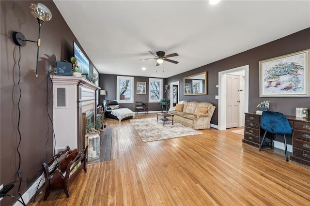 living area featuring light wood finished floors, ceiling fan, baseboards, and a glass covered fireplace