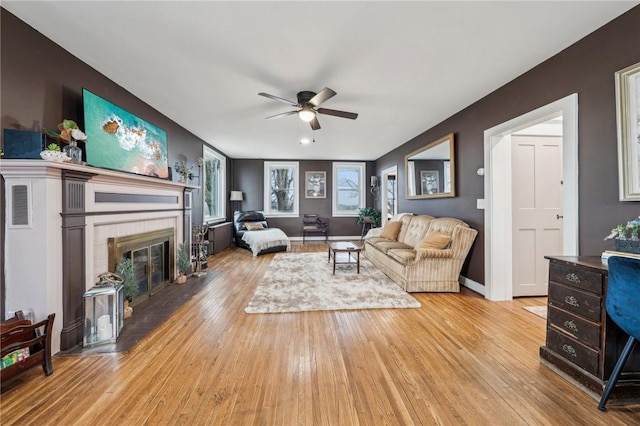 living area with wood-type flooring, a fireplace, baseboards, and a ceiling fan