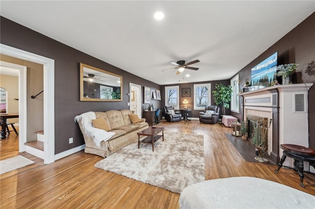 living room featuring a fireplace with flush hearth, ceiling fan, wood finished floors, and baseboards