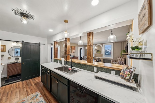 kitchen featuring pendant lighting, a barn door, a sink, wood finished floors, and dark cabinetry