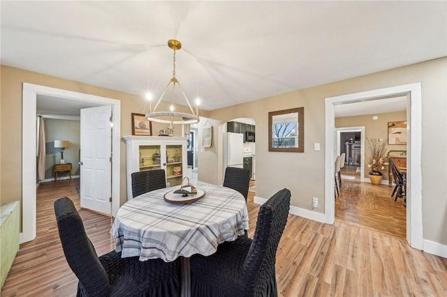 dining area featuring a chandelier, light wood-type flooring, arched walkways, and baseboards