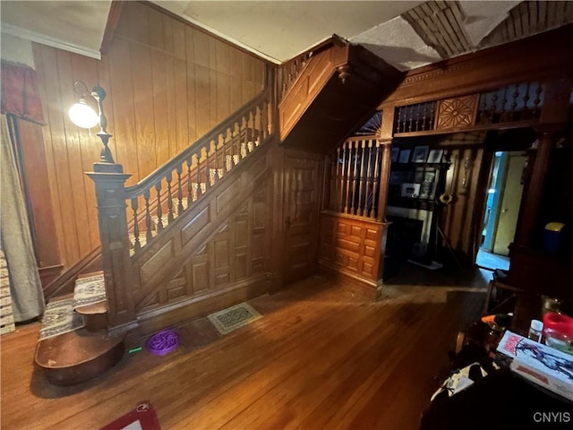 interior space with wooden walls, wood finished floors, visible vents, ornamental molding, and stairway