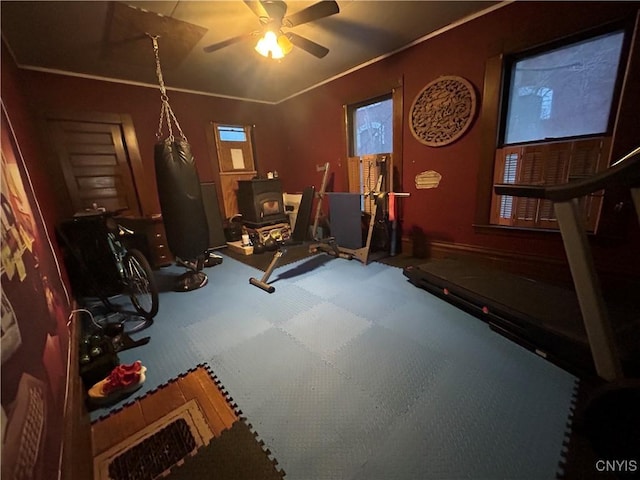 exercise room featuring a wood stove, a ceiling fan, and crown molding