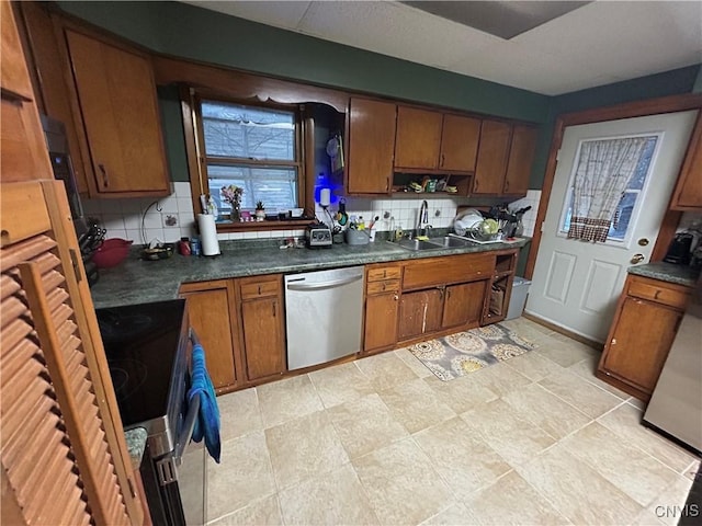 kitchen featuring a sink, appliances with stainless steel finishes, backsplash, brown cabinetry, and dark countertops