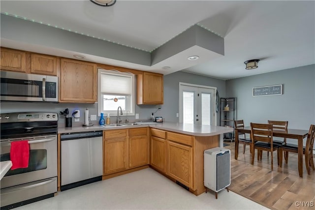 kitchen featuring appliances with stainless steel finishes, a peninsula, light countertops, a sink, and recessed lighting