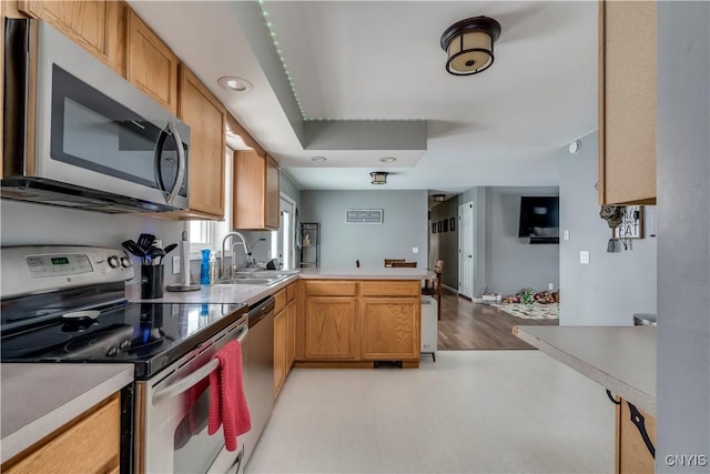 kitchen with stainless steel appliances, light countertops, a sink, and a peninsula