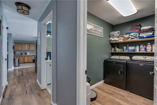 washroom featuring laundry area, baseboards, light wood-style floors, and washing machine and clothes dryer