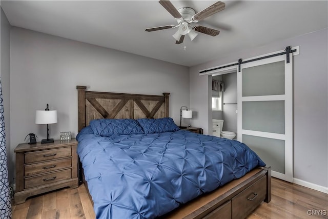 bedroom featuring a barn door, wood finished floors, a ceiling fan, and baseboards