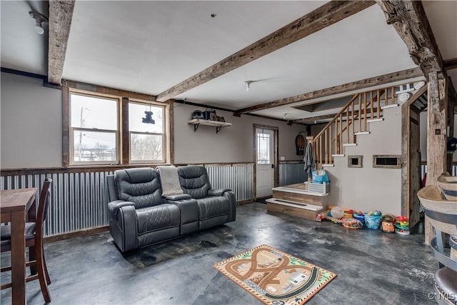 living room featuring unfinished concrete floors, beamed ceiling, and stairs