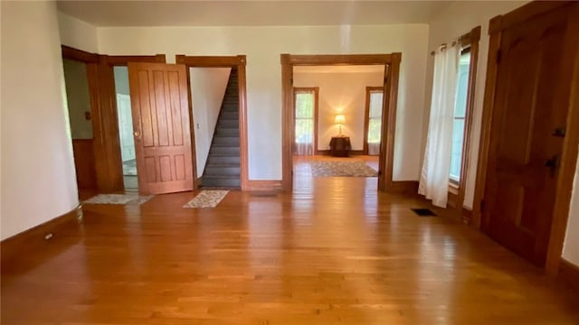 empty room with light wood-type flooring, visible vents, stairway, and baseboards