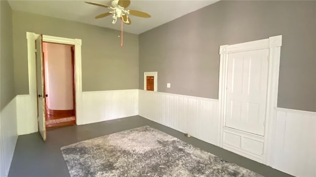 empty room featuring concrete flooring, a wainscoted wall, and ceiling fan