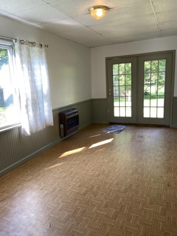 unfurnished living room with heating unit, a drop ceiling, and wainscoting