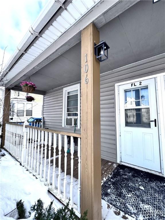 snow covered property entrance with cooling unit and a porch