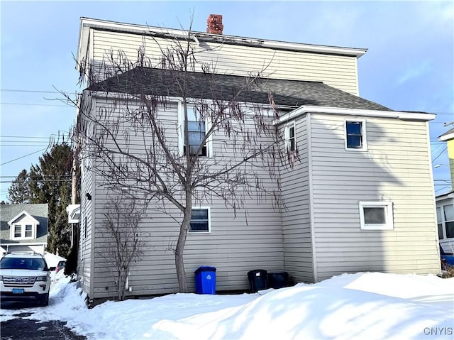 snow covered house featuring a chimney and a shingled roof