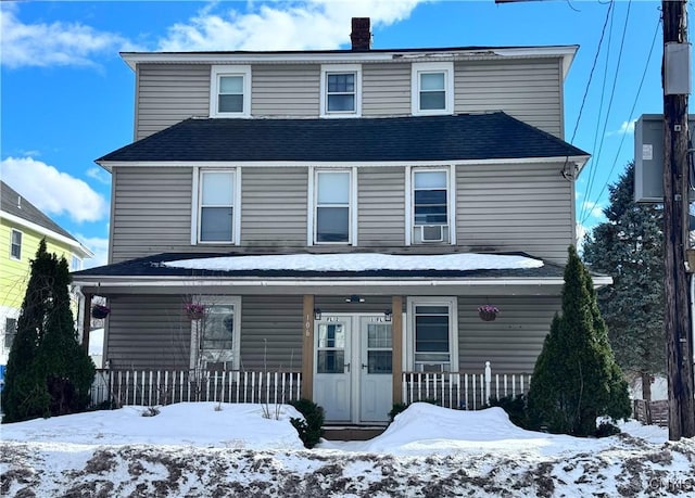 view of front of house featuring french doors, cooling unit, roof with shingles, covered porch, and a chimney