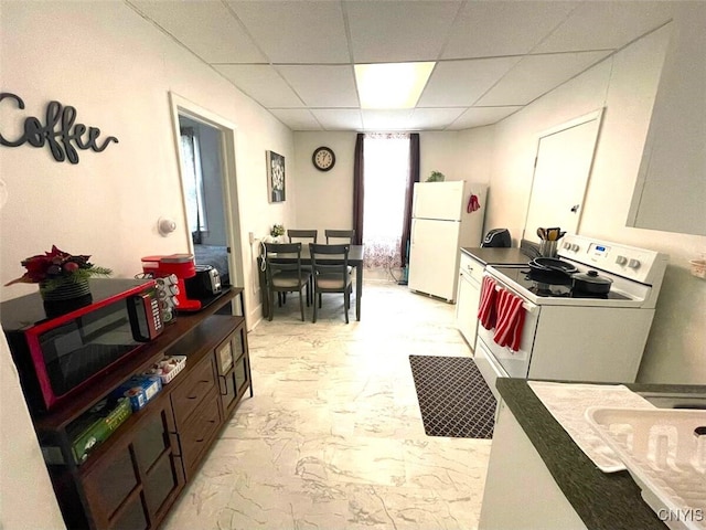 kitchen with a drop ceiling, white appliances, dark countertops, and marble finish floor