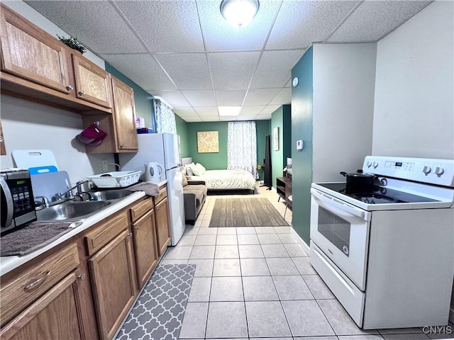 kitchen featuring white appliances, light tile patterned floors, brown cabinetry, a drop ceiling, and a sink