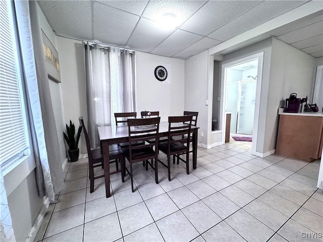 dining space with light tile patterned floors, a paneled ceiling, and baseboards