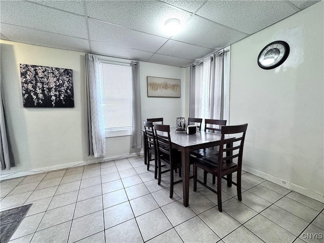 dining space featuring light tile patterned floors, a drop ceiling, and baseboards