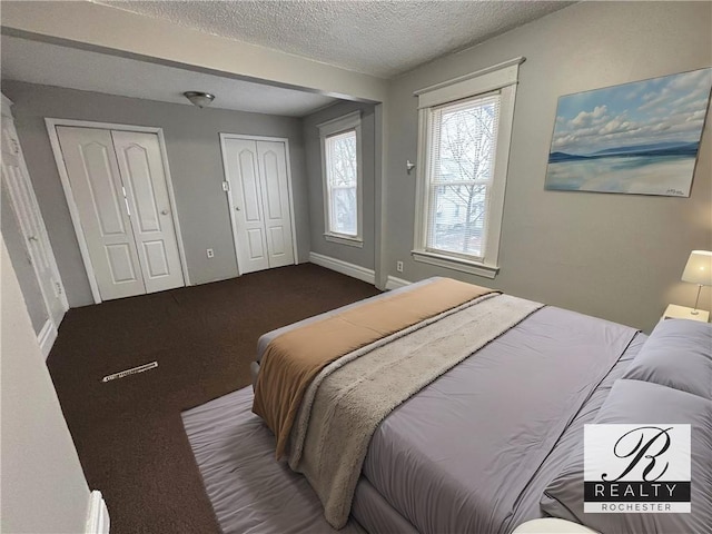 carpeted bedroom featuring multiple closets, a textured ceiling, and baseboards