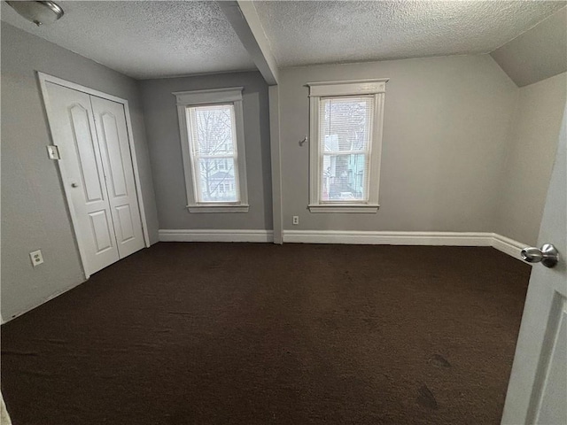 interior space with a textured ceiling, dark carpet, and baseboards