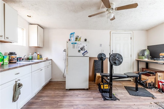 kitchen featuring light wood-style floors, freestanding refrigerator, white cabinets, a sink, and a textured ceiling