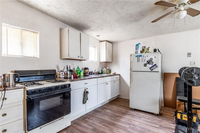 kitchen with light wood-type flooring, gas range, white cabinetry, and freestanding refrigerator