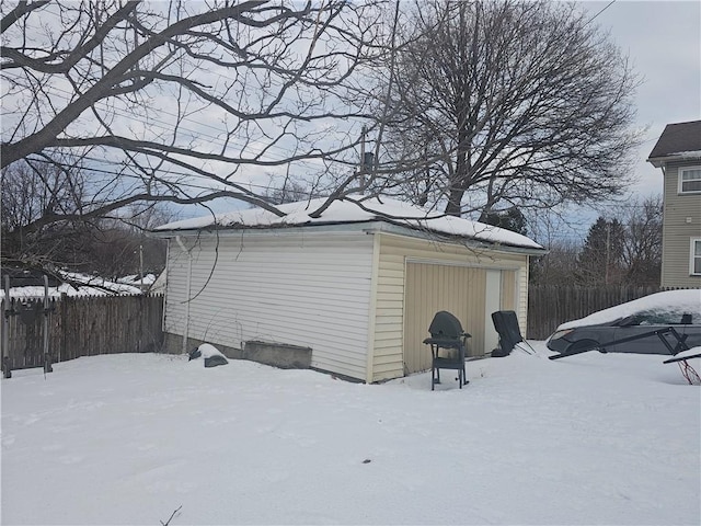 snow covered structure featuring fence and an outbuilding