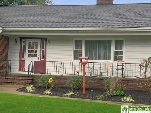 doorway to property featuring a porch, roof with shingles, and a chimney