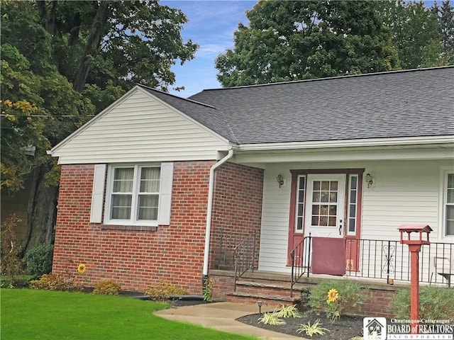 view of front of home with brick siding, roof with shingles, and a front yard