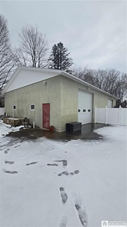 view of snow covered exterior featuring a garage and fence